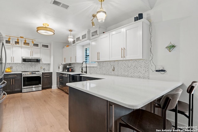 kitchen with decorative light fixtures, kitchen peninsula, appliances with stainless steel finishes, and white cabinetry