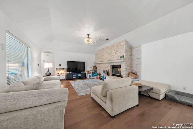 living room with hardwood / wood-style flooring, a notable chandelier, a stone fireplace, and vaulted ceiling