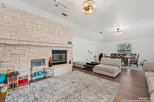 living room with track lighting, hardwood / wood-style floors, a stone fireplace, and a notable chandelier