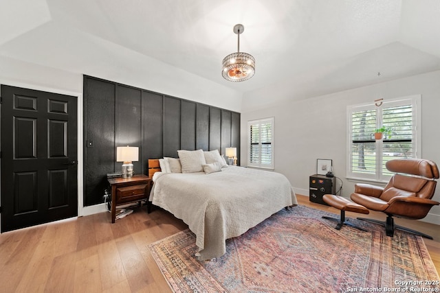 bedroom with multiple windows, a tray ceiling, an inviting chandelier, and light wood-type flooring