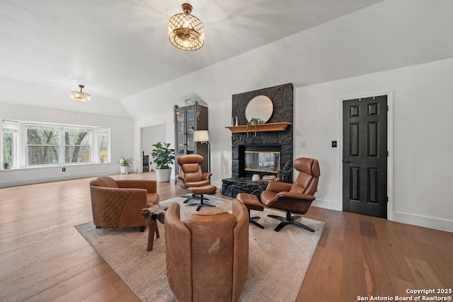 living room with a fireplace, lofted ceiling, a notable chandelier, and light wood-type flooring