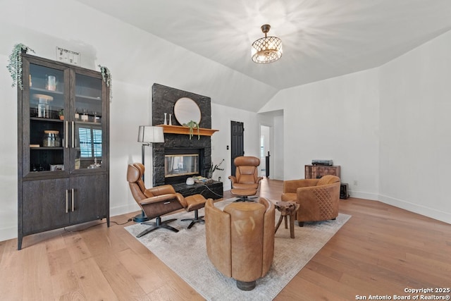 sitting room featuring lofted ceiling, a high end fireplace, an inviting chandelier, and light hardwood / wood-style floors