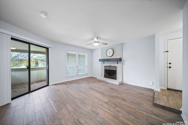 unfurnished living room featuring a brick fireplace, wood-type flooring, and ceiling fan