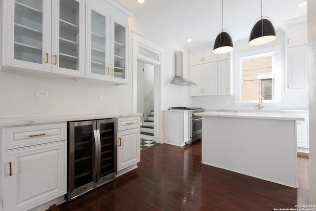 kitchen with high end stove, wine cooler, hanging light fixtures, wall chimney exhaust hood, and white cabinets