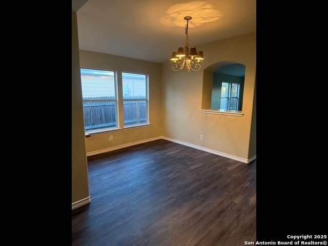 empty room featuring dark wood-type flooring and a chandelier