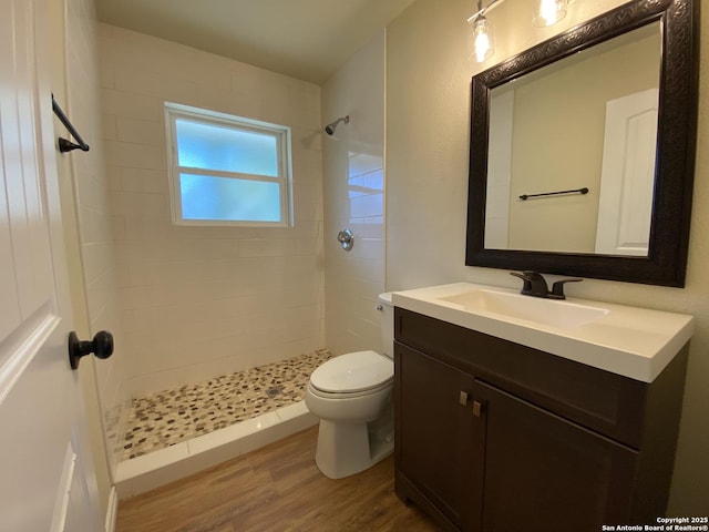 bathroom with toilet, a tile shower, hardwood / wood-style flooring, and vanity