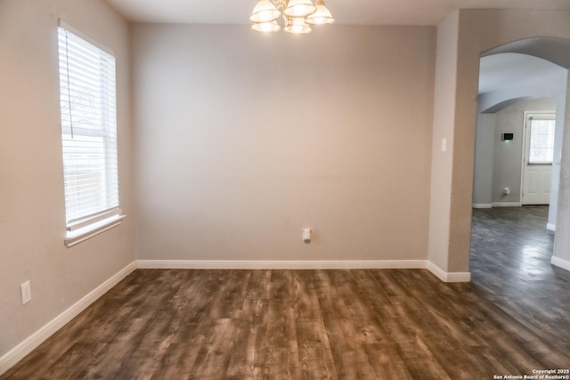 unfurnished room with dark hardwood / wood-style floors, a wealth of natural light, and an inviting chandelier