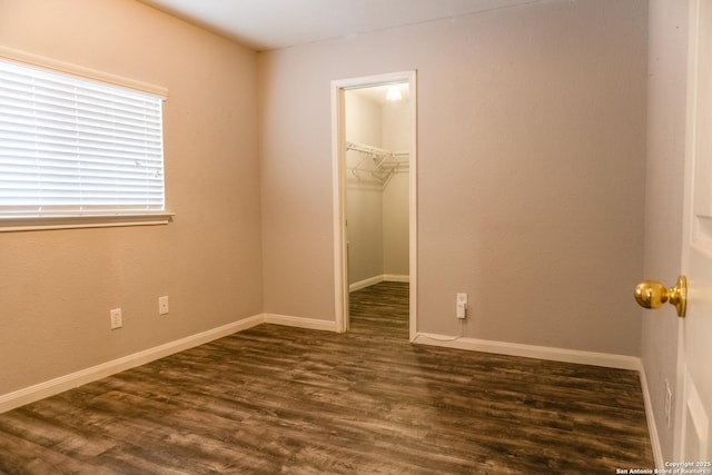 unfurnished bedroom featuring a walk in closet, a closet, and dark hardwood / wood-style flooring