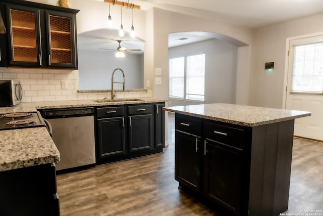 kitchen with appliances with stainless steel finishes, a kitchen island, decorative backsplash, sink, and ceiling fan