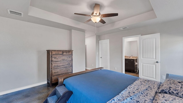 bedroom with ceiling fan, a raised ceiling, and ensuite bath