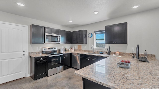 kitchen featuring kitchen peninsula, stainless steel appliances, a textured ceiling, light stone counters, and sink