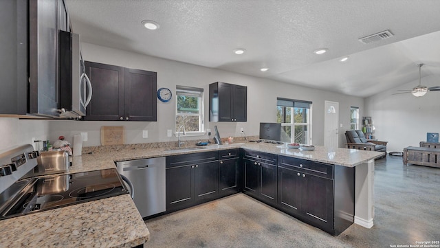 kitchen with vaulted ceiling, kitchen peninsula, stainless steel appliances, a textured ceiling, and light stone counters