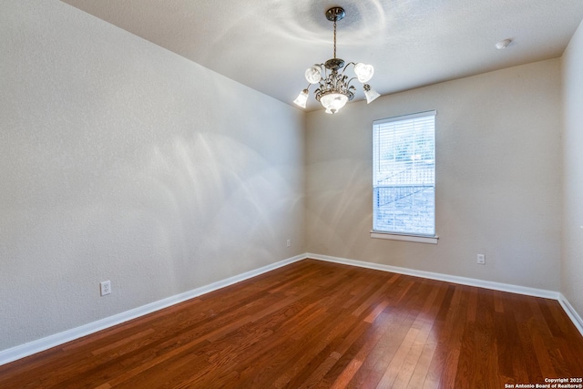 spare room featuring wood-type flooring and a chandelier