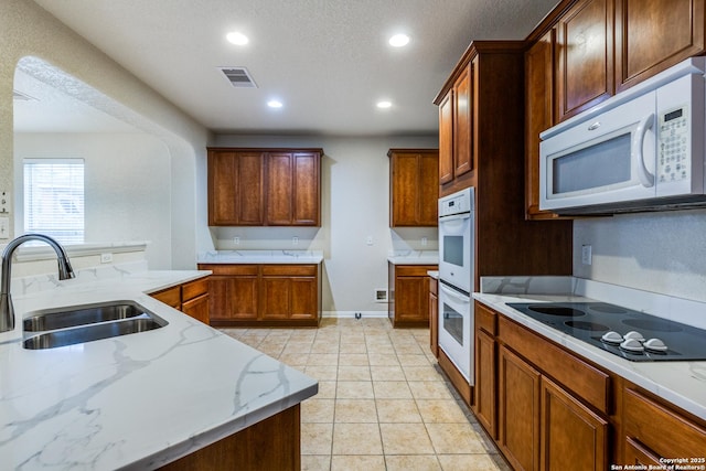 kitchen with sink, white appliances, a textured ceiling, light tile patterned floors, and light stone counters