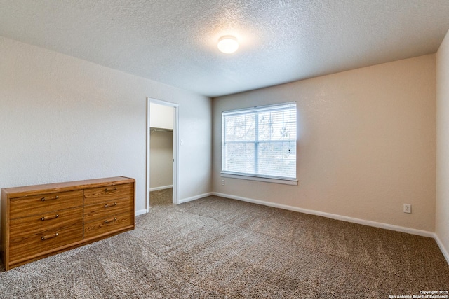 unfurnished bedroom with carpet, a closet, a spacious closet, and a textured ceiling