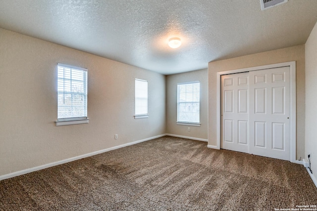 unfurnished bedroom with a closet, a textured ceiling, multiple windows, and carpet flooring