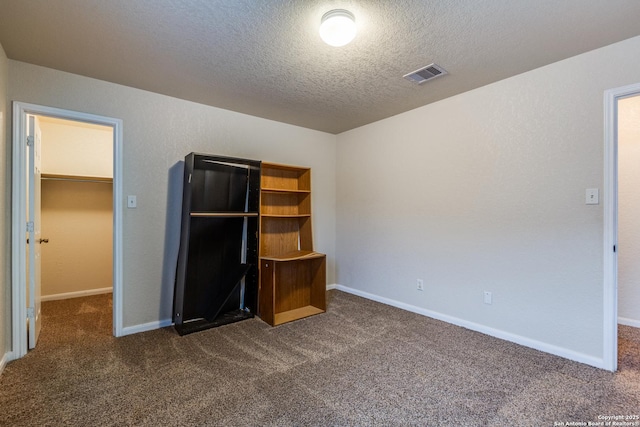 unfurnished bedroom featuring a closet, a spacious closet, dark carpet, and a textured ceiling