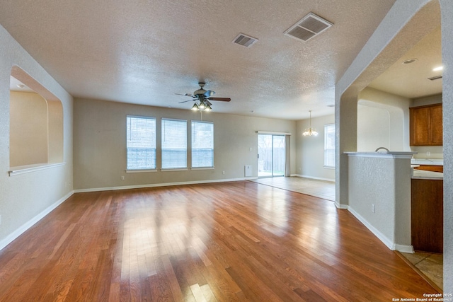 unfurnished living room featuring light wood-type flooring, ceiling fan with notable chandelier, and a textured ceiling