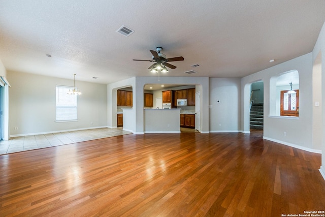 unfurnished living room featuring ceiling fan with notable chandelier, a textured ceiling, and light hardwood / wood-style flooring