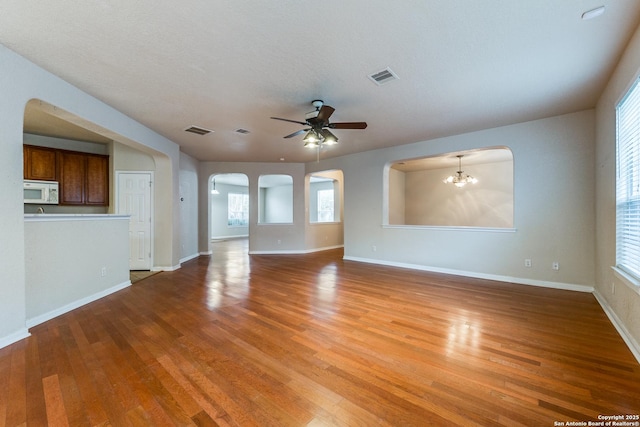 unfurnished living room featuring a textured ceiling, a wealth of natural light, ceiling fan with notable chandelier, and hardwood / wood-style flooring