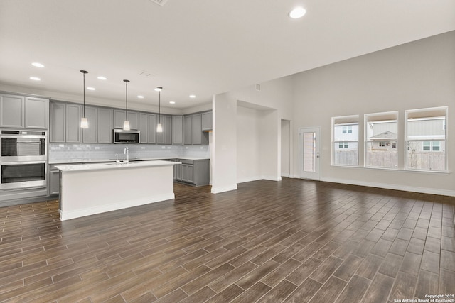 kitchen featuring appliances with stainless steel finishes, decorative backsplash, sink, gray cabinets, and a center island with sink