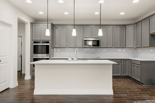 kitchen featuring stainless steel appliances, sink, hanging light fixtures, gray cabinets, and a kitchen island with sink