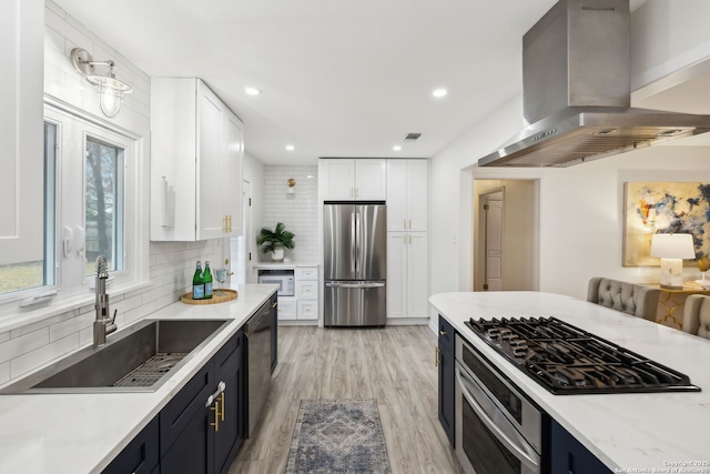 kitchen featuring sink, white cabinetry, appliances with stainless steel finishes, island exhaust hood, and backsplash