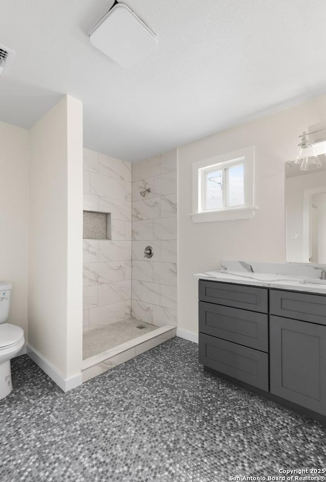 bathroom featuring toilet, a tile shower, and vanity