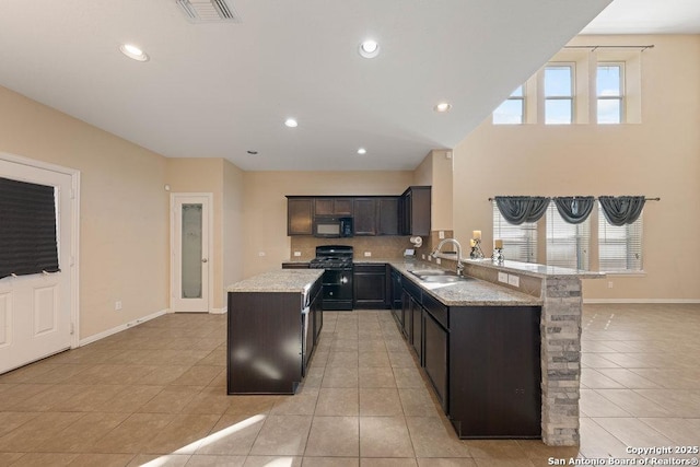 kitchen with a kitchen island, sink, light tile patterned floors, light stone counters, and range