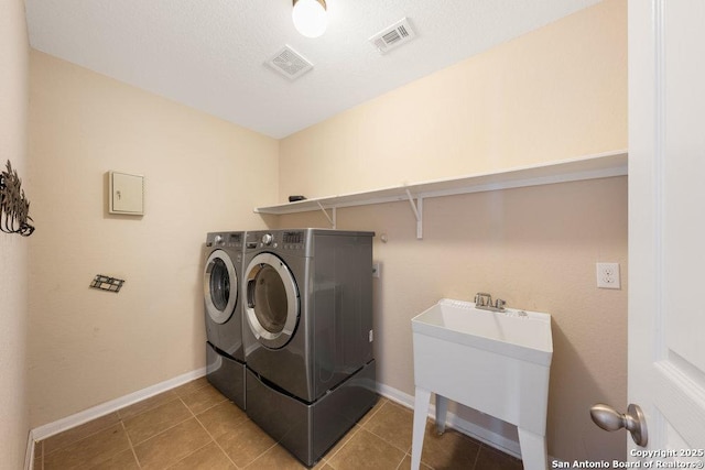 laundry area with a textured ceiling, independent washer and dryer, and light tile patterned flooring