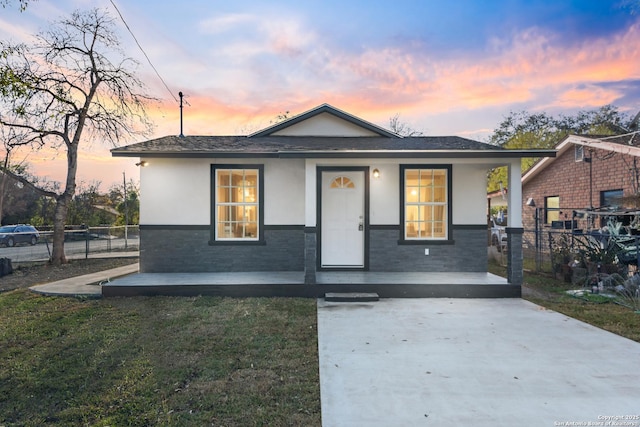 bungalow featuring fence, driveway, a porch, a yard, and stucco siding