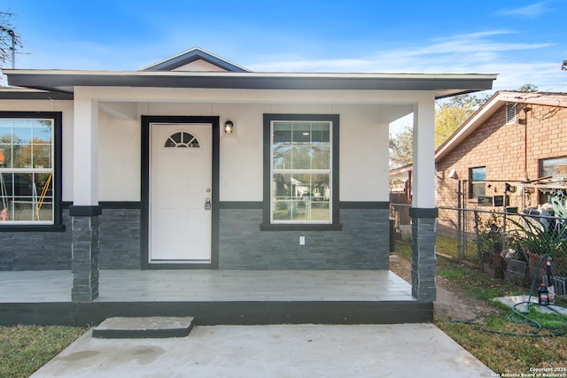 doorway to property featuring stone siding, stucco siding, a porch, and fence