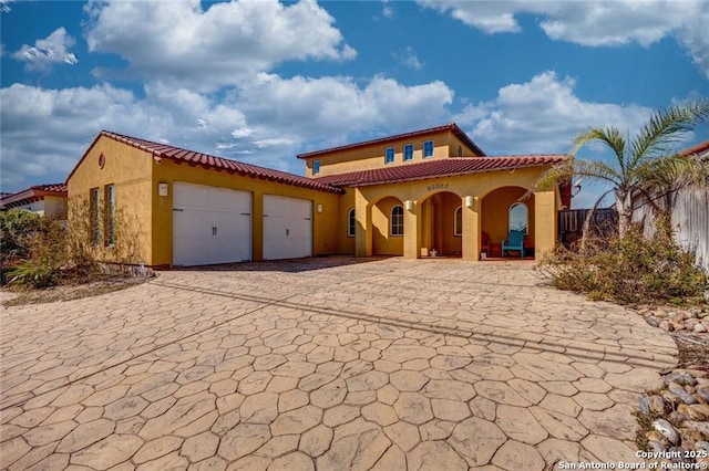 mediterranean / spanish home with an attached garage, a tile roof, and stucco siding