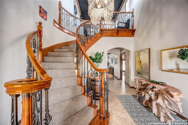 staircase with a chandelier, arched walkways, tile patterned flooring, and a towering ceiling