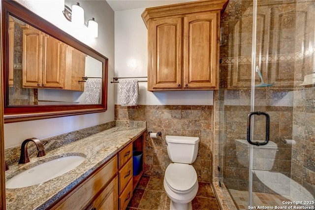 bathroom with toilet, vanity, tile walls, wainscoting, and a shower stall