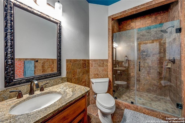 bathroom with toilet, a stall shower, tile walls, and vanity