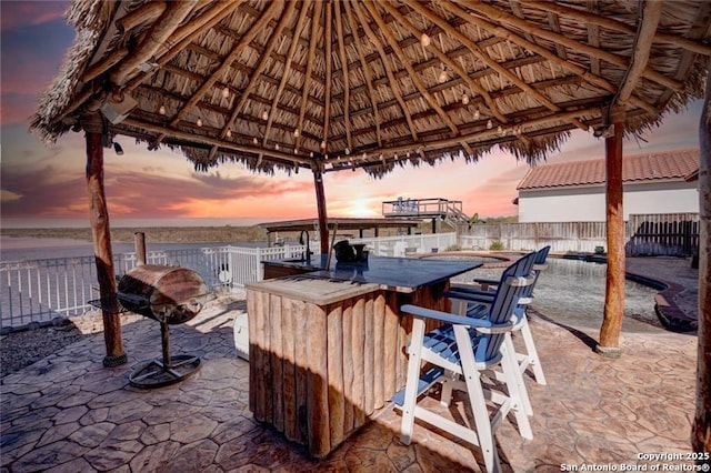 patio terrace at dusk featuring a water view, a gazebo, exterior bar, and grilling area