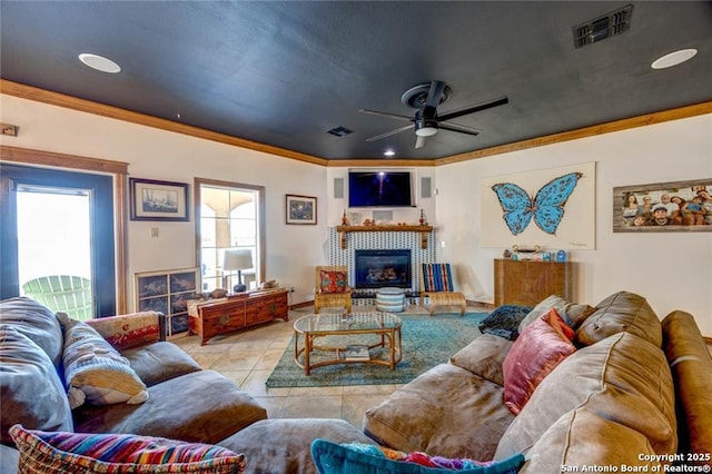 living room with light tile patterned floors, a tile fireplace, crown molding, and a healthy amount of sunlight