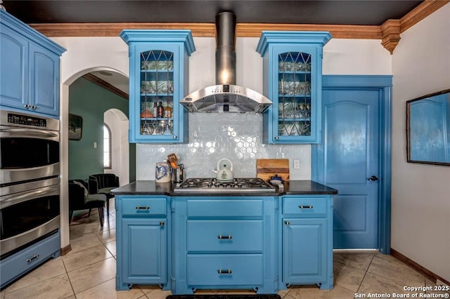 kitchen featuring wall chimney range hood, stainless steel appliances, blue cabinetry, backsplash, and crown molding