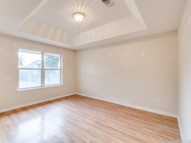 empty room featuring a tray ceiling and light hardwood / wood-style flooring