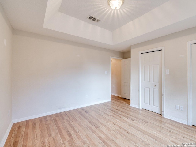 unfurnished bedroom featuring light hardwood / wood-style floors and a raised ceiling