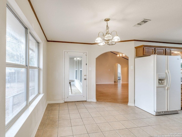 kitchen with light tile patterned floors, a wealth of natural light, white refrigerator with ice dispenser, and a chandelier