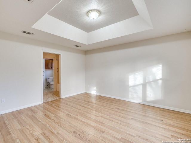 unfurnished room with a textured ceiling, a raised ceiling, and light wood-type flooring