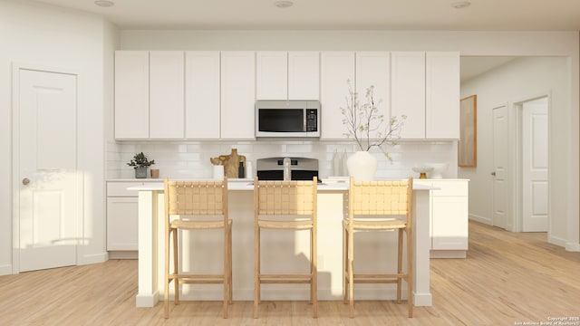 kitchen with white cabinetry, a kitchen bar, decorative backsplash, light wood-type flooring, and range