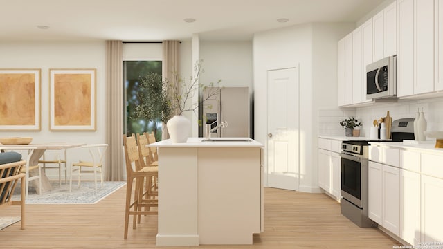 kitchen featuring appliances with stainless steel finishes, white cabinets, a center island with sink, and a kitchen bar