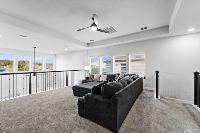 living room with ceiling fan, carpet floors, and a raised ceiling