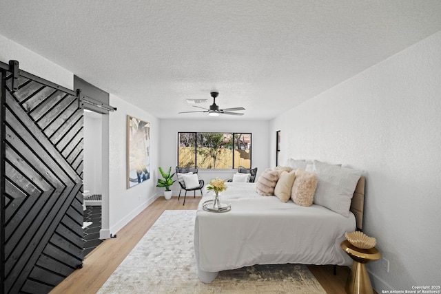 bedroom featuring ceiling fan, a barn door, a textured ceiling, and light hardwood / wood-style flooring