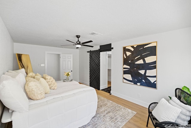 bedroom with ceiling fan, a textured ceiling, light hardwood / wood-style flooring, and a barn door