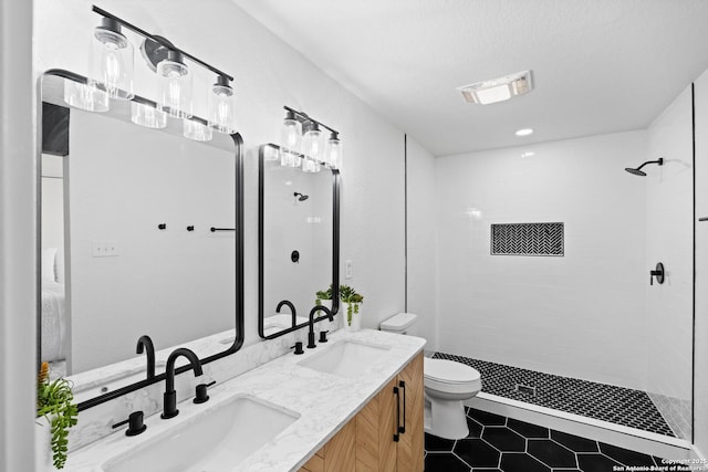 bathroom featuring toilet, vanity, a textured ceiling, and a tile shower