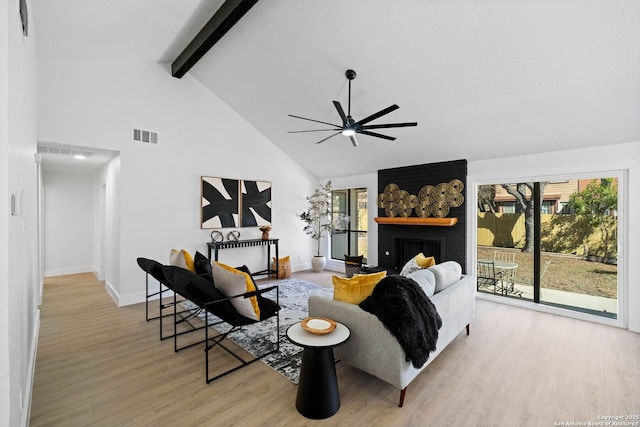 living room with ceiling fan, high vaulted ceiling, light wood-type flooring, a brick fireplace, and beam ceiling